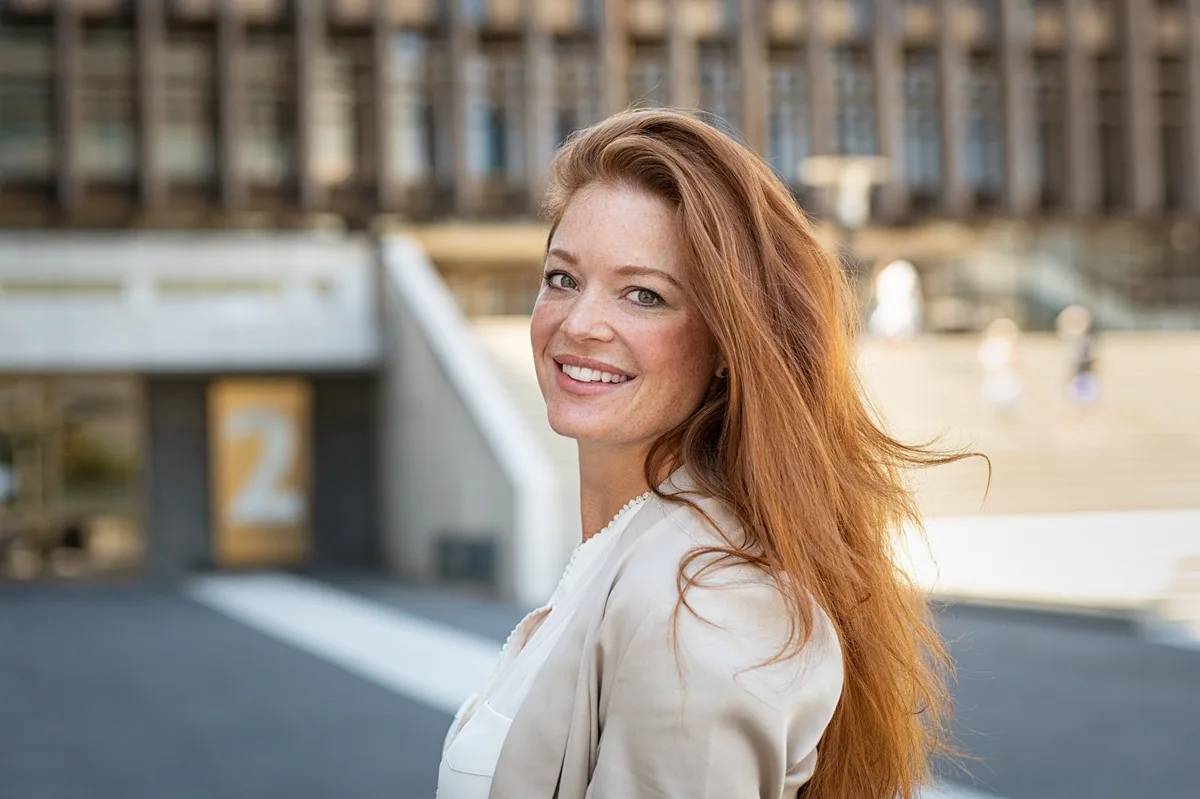 Red-haired woman smiling outdoors with natural beauty