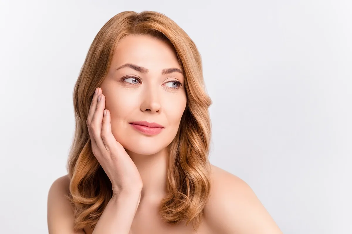 Red-haired woman touching face with healthy skin