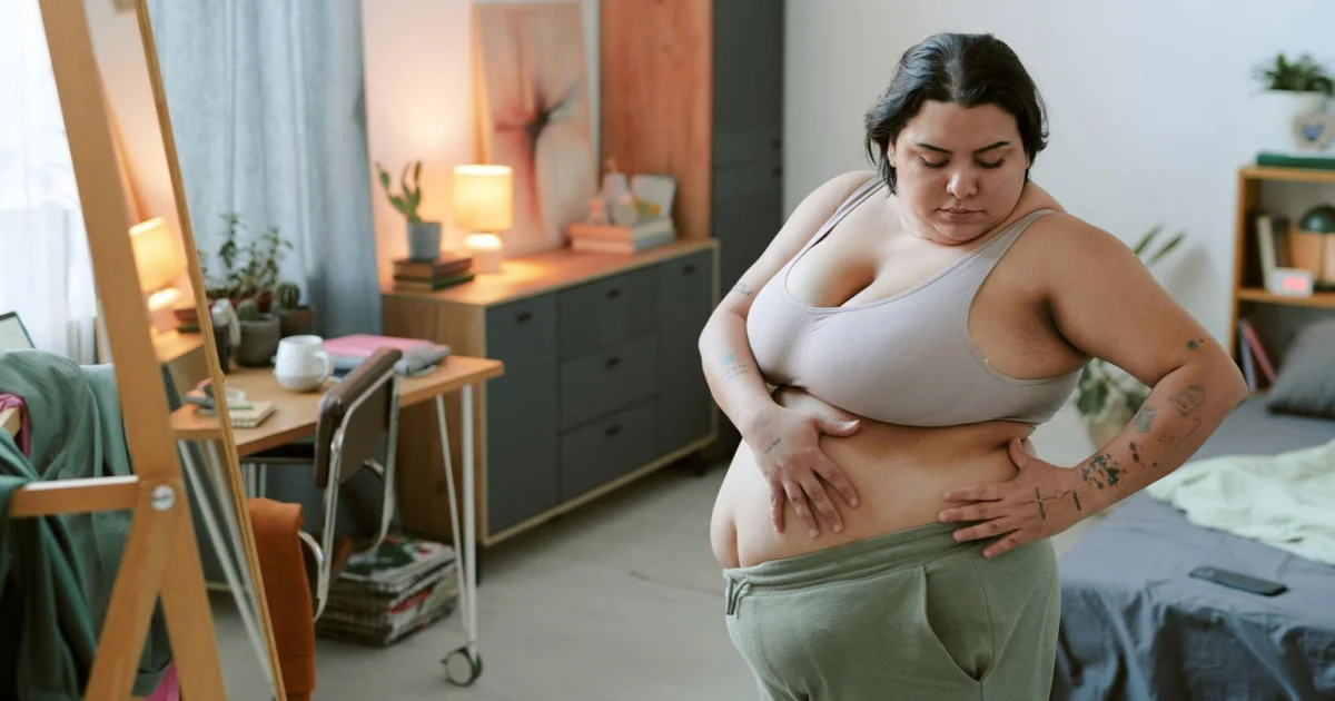 Woman in workout clothing looking thoughtfully at her waist while considering body contouring options